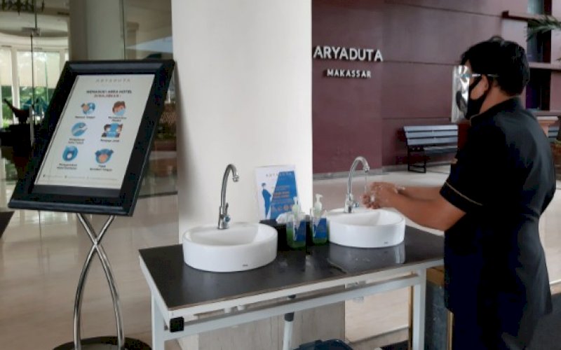 PROTOKOL KESEHATAN. Karyawan hotel sedang mencuci tangan di tempat yang tersedia di depan pintu masuk Hotel Aryaduta Makassar, Jumat (17/7/2020). Hotel ini menerapkan standar protokol kesehatan sejak awal sesuai anjuran pemerintah. foto: doelbeckz/pluz.id