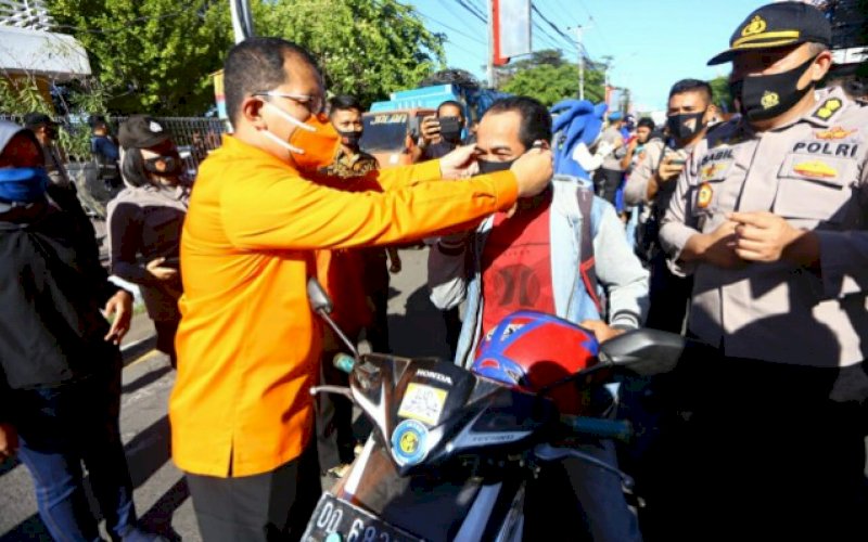 PAKAIKAN MASKER. Bakal calon Wali Kota Makassar, Mohammad Ramdhan Pomanto, memakaikan masker kepada salah satu pengendara motor pada kampanye melawan Covid-19 yang diselenggarakan Polda Sulsel di Jl Ahmad Yani, Kota Makassar, Kamis (10/9/2020). foto: istimewa