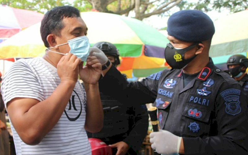 PASANGKAN MASKER. Danyon C Pelopor Satbrimob Polda Sulsel, Kompol Nur Ichsan, memasangkan masker kepada salah satu warga pada operasi yustisi protokol kesehatan Covid-19 di Bone, Jumat (5/2/2021). foto: humas brimob bone