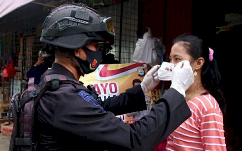 PASANGKAN MASKER. Personel Batalyon C Pelopor Satbrimob Polda Sulsel memasangkan masker kepada salah satu warga saat patroli imbauan masyarakat di pasar sentral lama Watampone, Minggu (21/2/2021). foto: humas brimob bone
