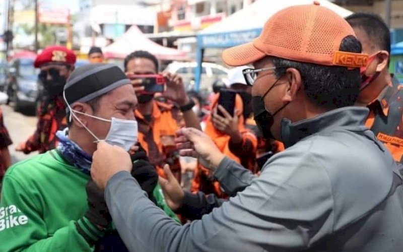 PASANGKAN MASKER. Wali Kota Makassar, Moh Ramdhan Pomanto, memasangkan masker kepada salah satu pengendara yang lewat di depan Pasar Antang, Kecamatan Manggala, Minggu (15/8/2021). foto: istimewa