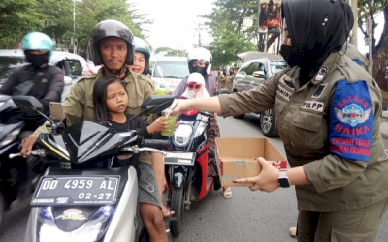 BERBAGI. Personel Satpol PP Kota Makassar membagikan ratusan takjil buka puasa kepada setiap pengendara yang melintas di pintu masuk Anjungan Pantai Losari Makassar, Rabu (20/4/2022). foto: istimewa