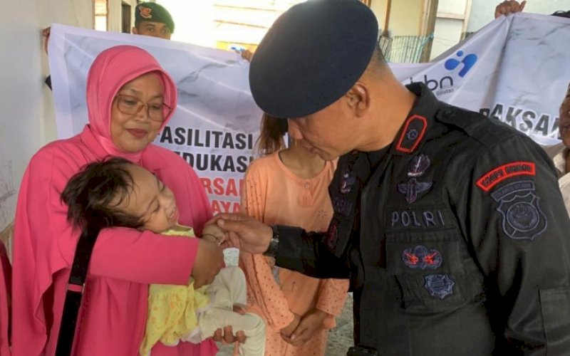 BAKTI SOSIAL. Danyon C Pelopor Sat Brimob Polda Sulsel, Kompol Nur Ichsan, menyapa seorang balita saat ikut bakti sosial pembagian makanan penambah gizi untuk balita dan ibu hamil di Kabupaten Bone, Rabu (22/3/2023). foto: istimewa
