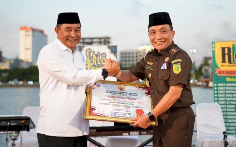 PENGHARGAAN. Pj Gubernur Sulsel, Bahtiar Baharuddin, memberikan piagam penghargaan kepada Leonard Eben Ezer Simanjuntak atas dedikasi dan pengabdiannya selama menjabat Kajati Sulsel di Kawasan Wisata Kuliner Lego-lego Center Point of Indonesia (CPI) Makassar, Rabu (20/3/2024). foto: istimewa