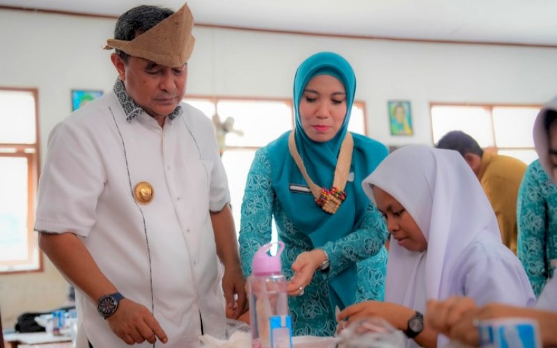 MENYAJIKAN. Pj Gubernur Sulbar Bahtiar Baharuddin bersama Pj Ketua Tim Penggerak PKK Provinsi Sulbar Sofha Marwah Bahtiar menyajikan makanan saat memantau jalannya uji coba program Makan Bergizi Gratis di SMAN 1 Pasangkayu, Senin (11/11/2024). foto: istimewa