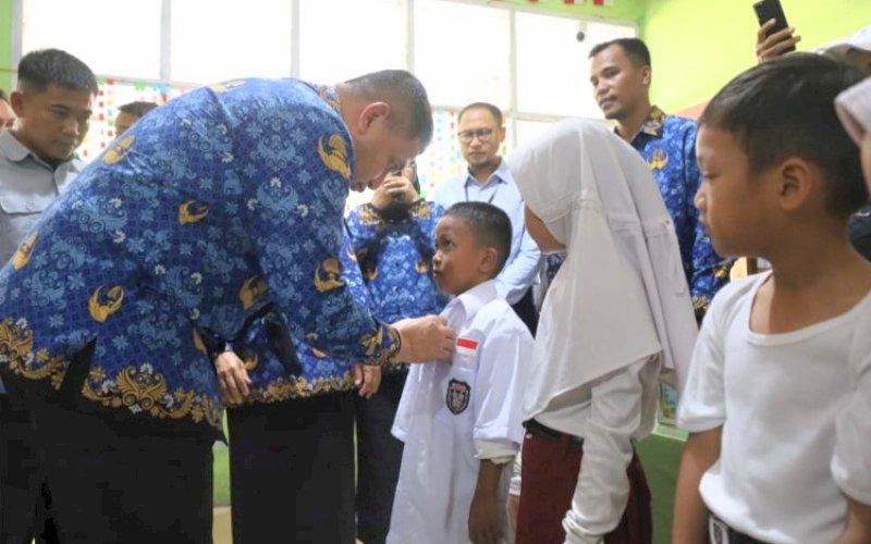 PEMASANGAN. Wali Kota Makassar, Munafri Arifuddin, memasangkan pakaian kepada salah satu siswa di sela-sela penyerahan seragam sekolah gratis di SD Inpres Cambaya I, II, dan III, Kecamatan Tallo, Kota Makassar, Senin (17/11/2025). foto: istimewa